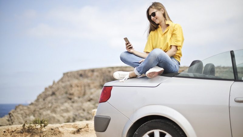 Frau sitzt auf Auto mit Strand im Hintergrund