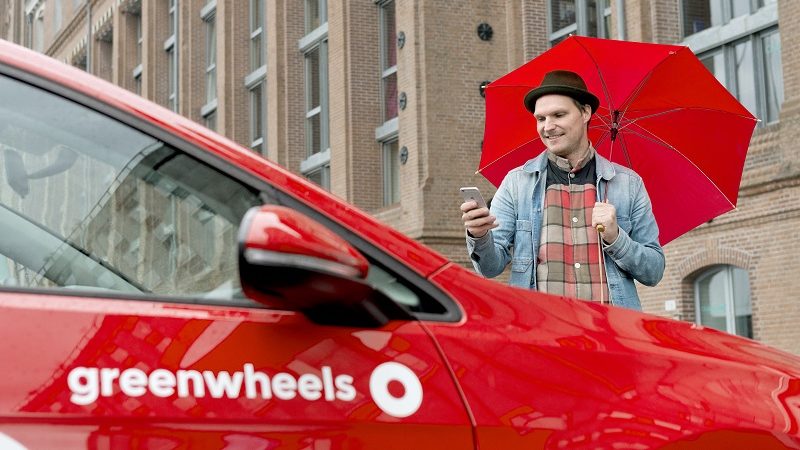 Greenwheels Carsharing Auto mit Logo und Mann mit Regenschirm
